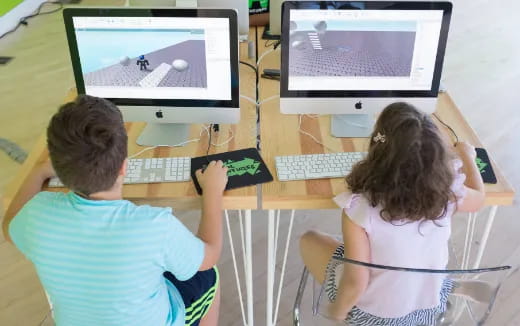 a couple of kids sitting at a computer desk