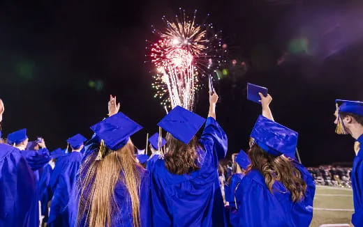 a group of people in graduation gowns and caps holding up fireworks