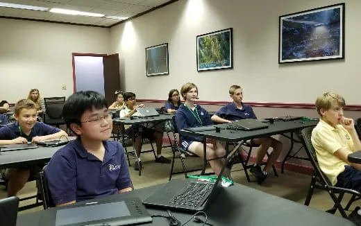 a group of children sitting at desks with laptops