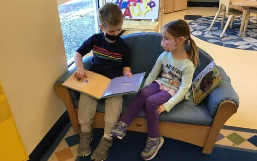 a boy and girl sitting on a couch looking at a laptop