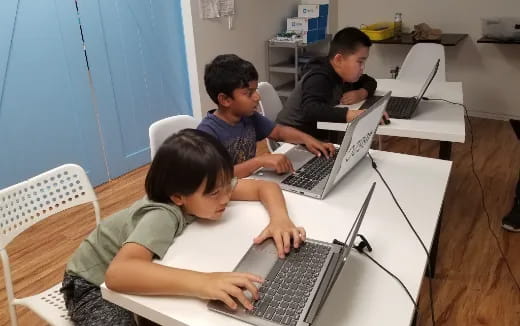 a group of boys sitting at a table with laptops