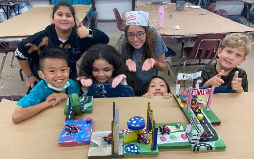 a group of children sitting at a table with a toy