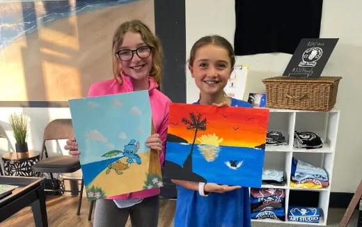 a couple of girls holding paintings