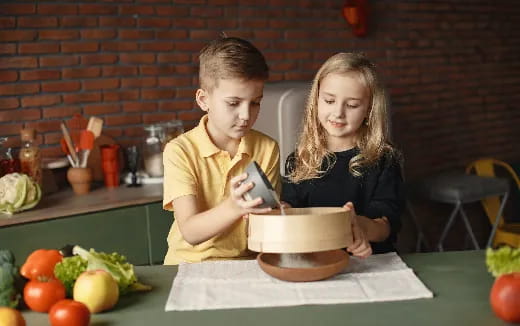a boy and girl sitting at a table with a bowl of food
