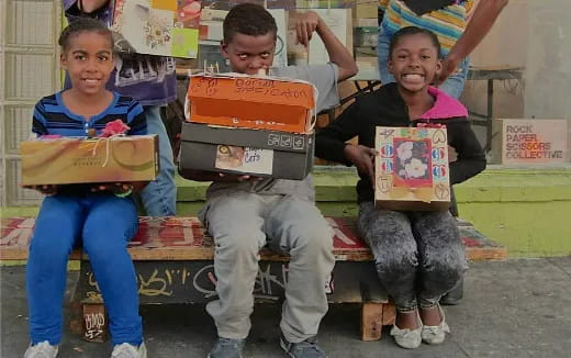 a group of kids sitting on a bench with boxes on their heads
