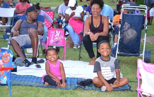 a group of people sitting on a blanket in a park