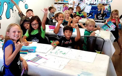 a group of children sitting at a table with a white board