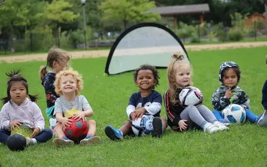 a group of kids sitting on the grass with helmets