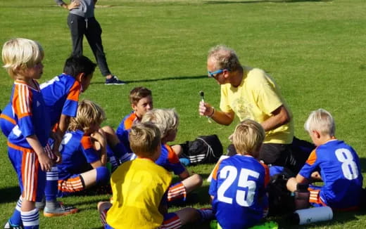 a person talking to a group of kids on a field