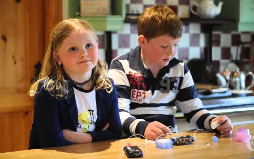 a boy and girl sitting at a table with a game controller