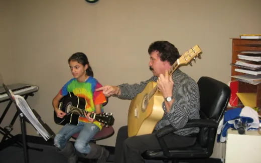 a man playing a guitar next to a woman sitting in a chair