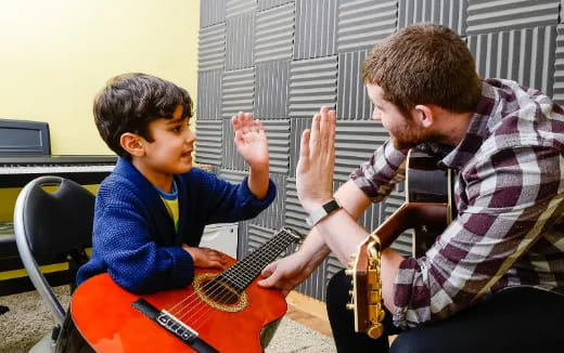 a person playing guitar to a boy