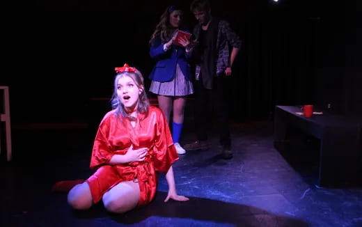 a girl in a red dress on a stage with other people