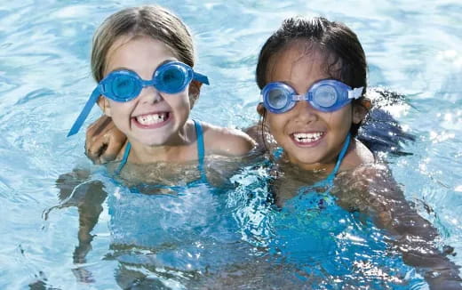 a couple of girls wearing goggles and swimming in a pool