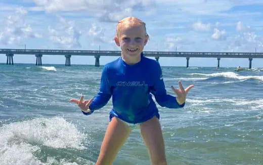 a boy in a blue shirt in the water with a pier in the background