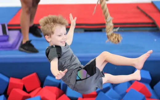 a boy sitting on a red and blue chair with his arms up