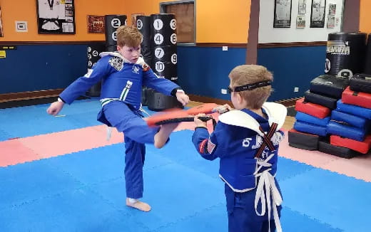 a couple of boys in blue karate uniforms holding swords