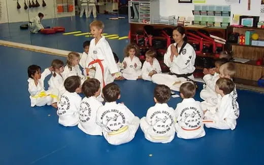 a group of children in white karate uniforms sitting on a blue mat