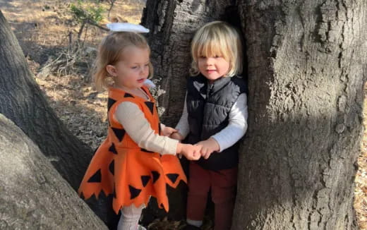 two children standing next to a tree