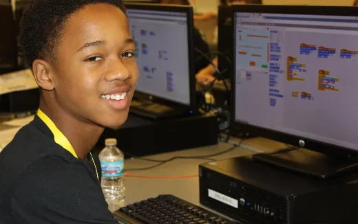 a boy smiling and sitting at a computer desk