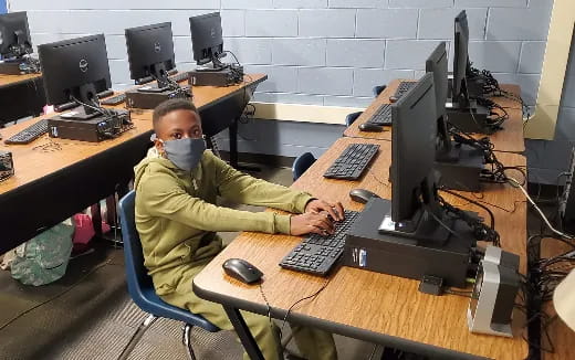 a boy sitting at a desk with a computer and a mask on