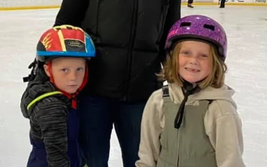 a couple of children wearing helmets and standing on ice