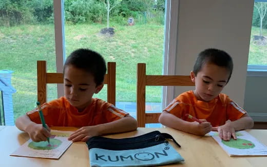 a couple of boys sitting at a table writing on paper