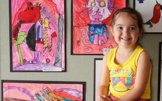 a girl standing next to several paintings