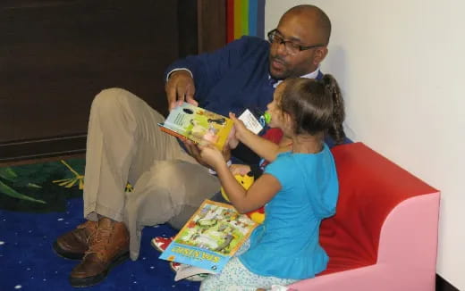 a person and a child sitting on a couch reading a book