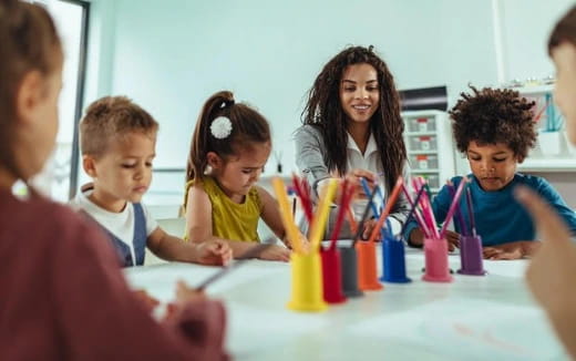 a group of children sitting at a table with colored pencils