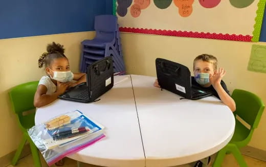 a couple of kids eating at a table with a laptop
