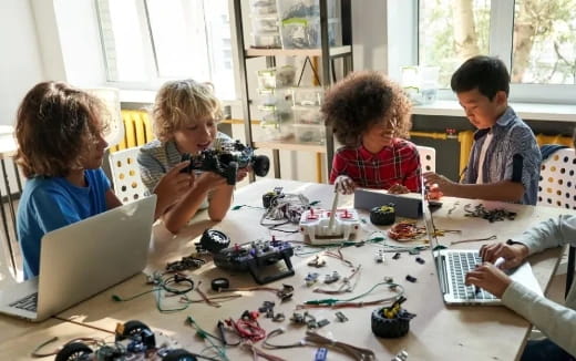 a group of kids sitting around a table with laptops and toys