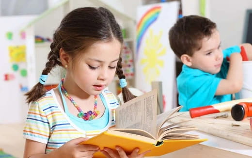 a young girl reading a book to a young boy