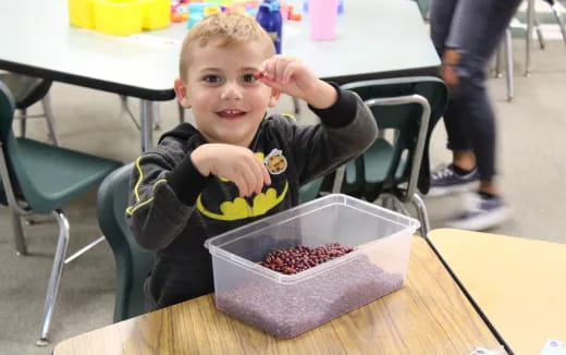 a boy sitting at a table with a container of food