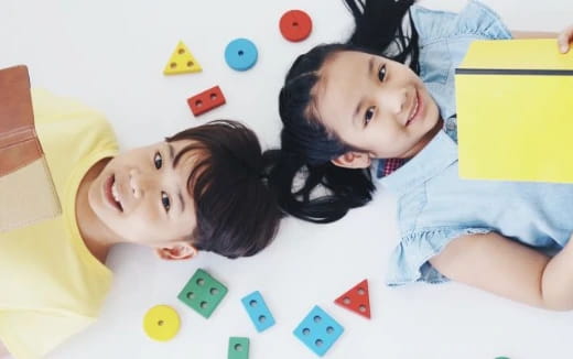 a couple of girls lying on a bed with colorful blocks