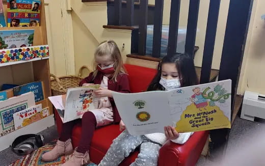 a couple of girls sitting on a couch reading books