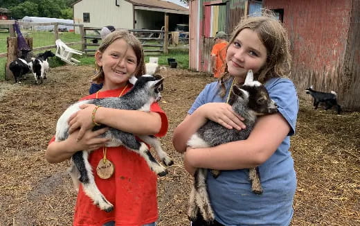 a couple of girls holding a baby goat