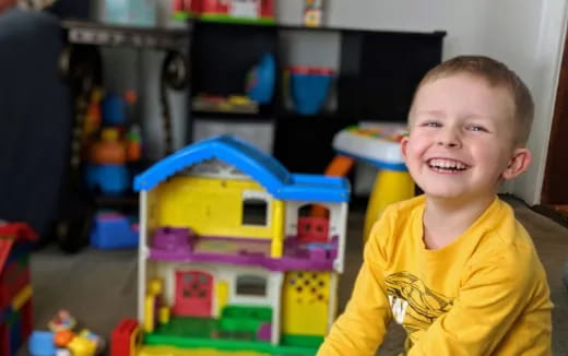 a boy smiling in front of a toy house