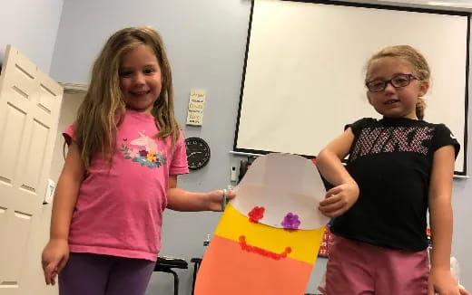 a couple of girls standing next to a cake