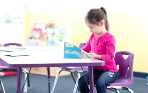 a girl sitting at a table looking at a tablet