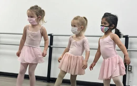 a group of girls wearing pink dresses and masks