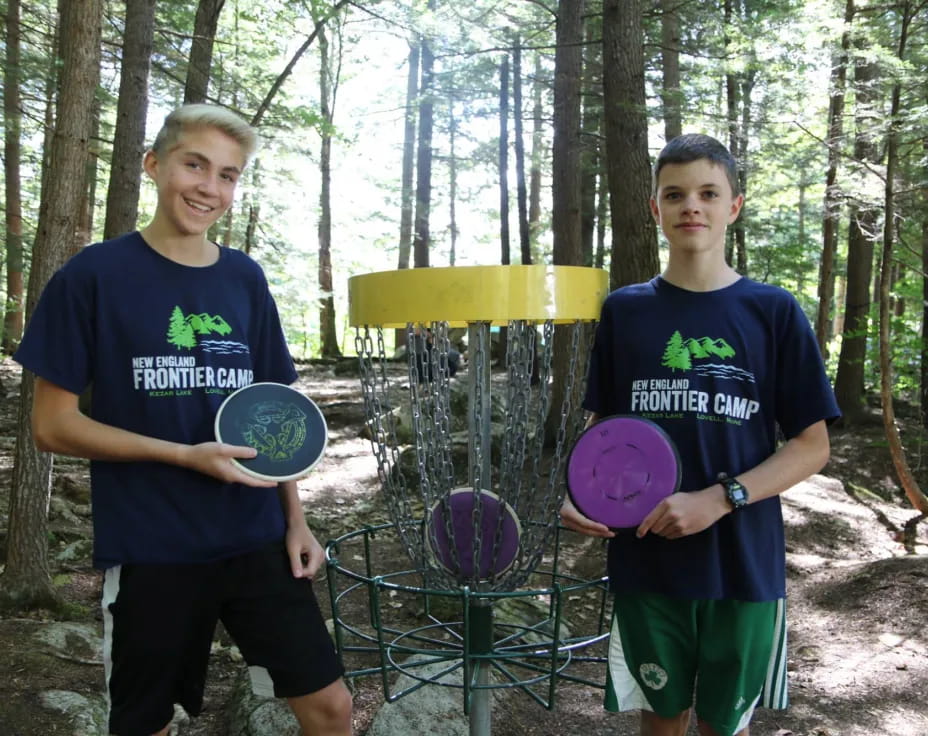 a couple of boys holding frisbees in a park