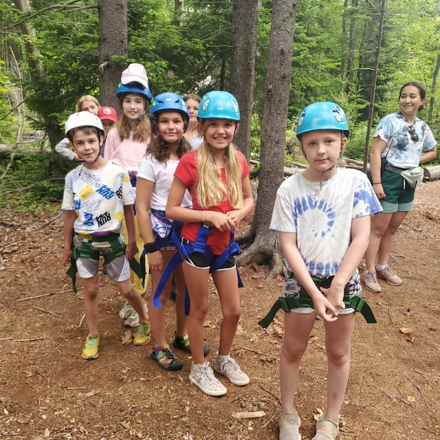 a group of kids wearing helmets and standing in the woods
