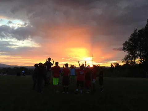 a group of people standing in a field with a sunset in the background