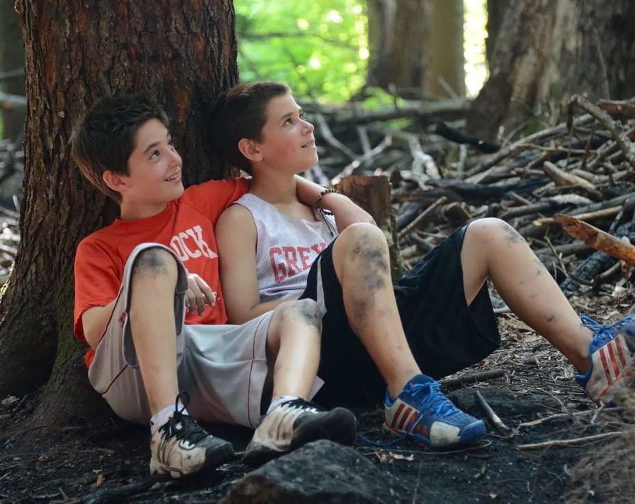 a couple of boys sitting on a tree branch