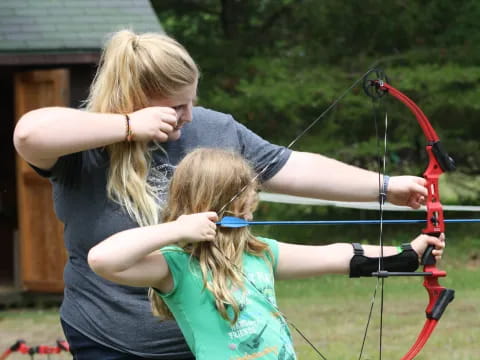 a woman helping a girl play a bow and arrow