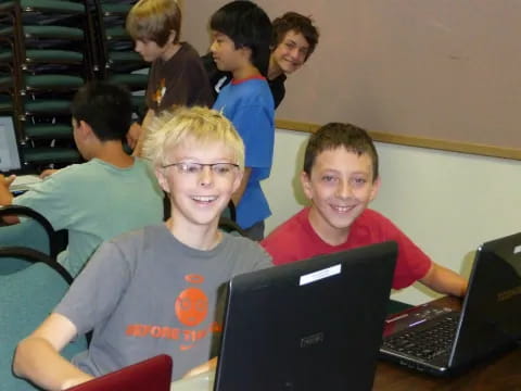 a group of boys sitting at a table with laptops