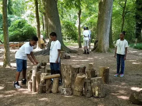 a group of people standing around a stack of wood in a forest