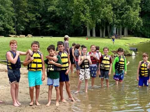 a group of boys in life vests standing in a body of water