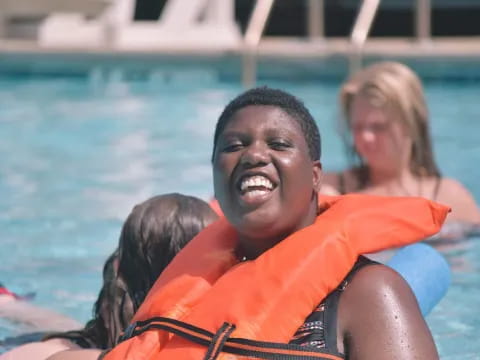 a boy in an orange life jacket in a pool with a woman in the background